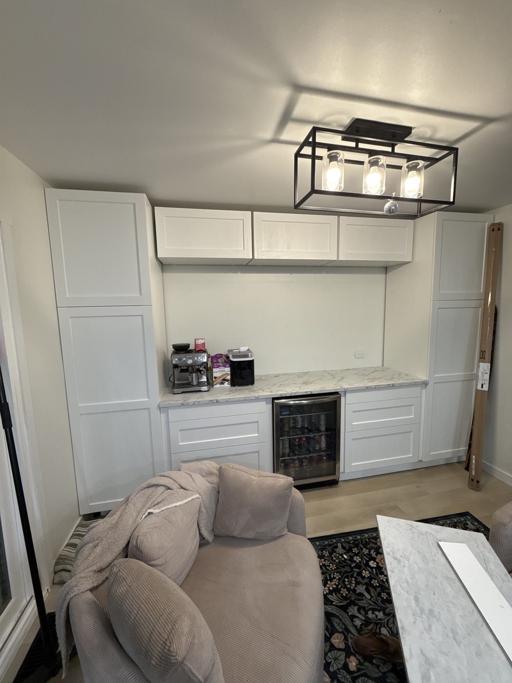 Finished basement bar with white shaker cabinets, marble counter, beverage fridge and espresso station